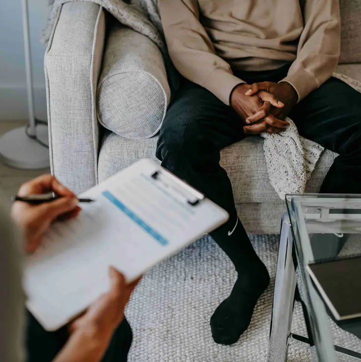 A therapist taking notes on a clipboard while a client sits on a couch